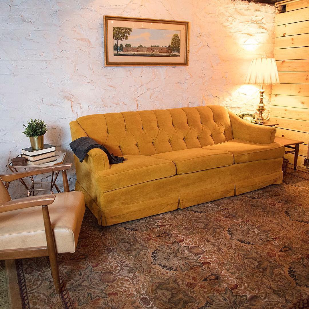 Cozy basement room with mustard yellow couch, vintage rug, and soft lighting.